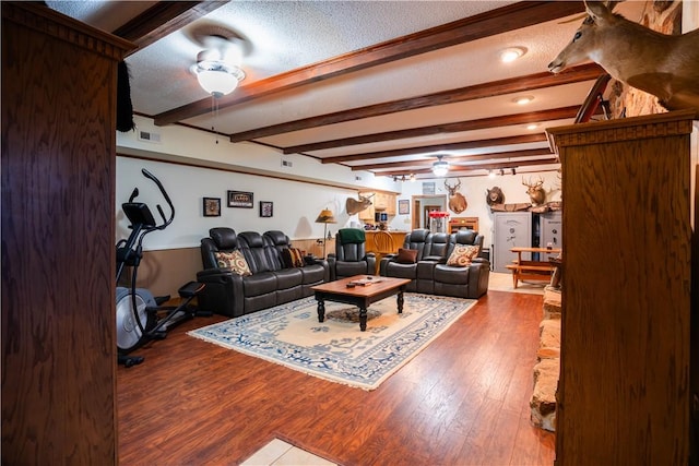 living room featuring ceiling fan, beam ceiling, wood-type flooring, and a textured ceiling