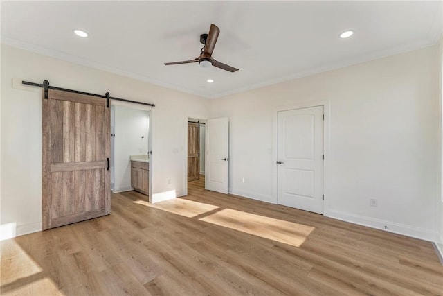 unfurnished bedroom with connected bathroom, light hardwood / wood-style floors, a barn door, and ceiling fan