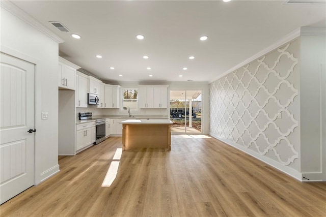 kitchen featuring a kitchen island, appliances with stainless steel finishes, white cabinetry, crown molding, and light hardwood / wood-style flooring