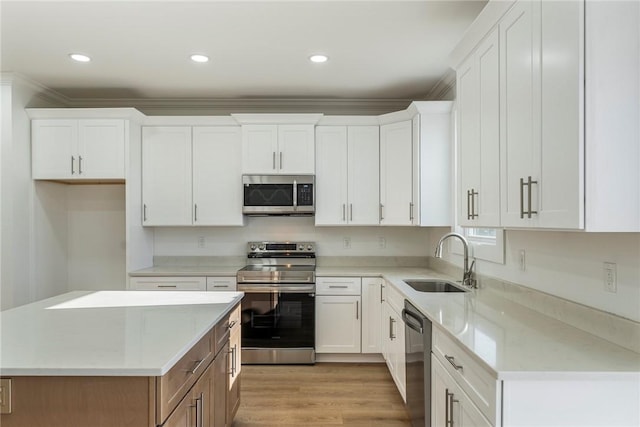 kitchen featuring sink, appliances with stainless steel finishes, white cabinetry, light hardwood / wood-style floors, and a kitchen island