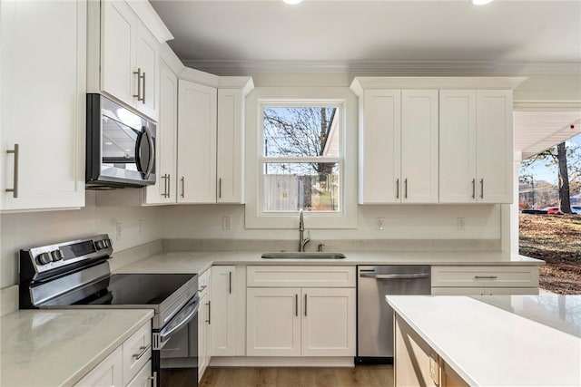 kitchen with sink, appliances with stainless steel finishes, white cabinetry, ornamental molding, and light wood-type flooring