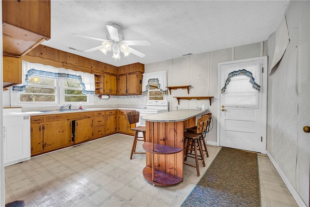 kitchen with sink, ceiling fan, a kitchen breakfast bar, white range with electric stovetop, and a textured ceiling