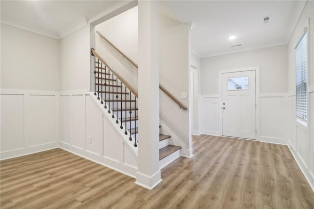 foyer with a healthy amount of sunlight, ornamental molding, and light wood-type flooring