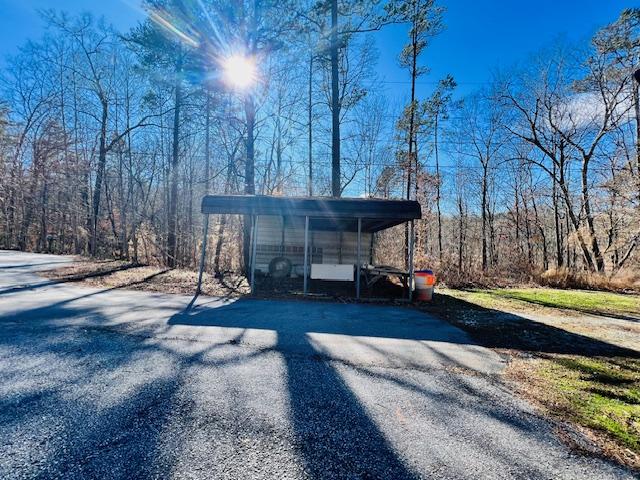 view of outbuilding featuring aphalt driveway, a detached carport, and a view of trees