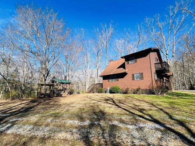 view of side of home featuring a balcony, a chimney, and a yard