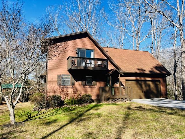 chalet / cabin featuring a garage, a balcony, concrete driveway, and a front yard