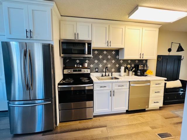 kitchen featuring appliances with stainless steel finishes, white cabinetry, sink, backsplash, and light hardwood / wood-style floors