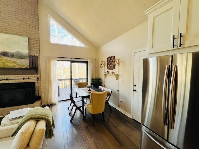 dining area with dark wood-style floors, a fireplace, a textured ceiling, high vaulted ceiling, and baseboards