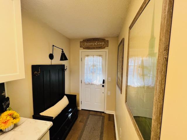 doorway featuring a textured ceiling, dark wood finished floors, and baseboards