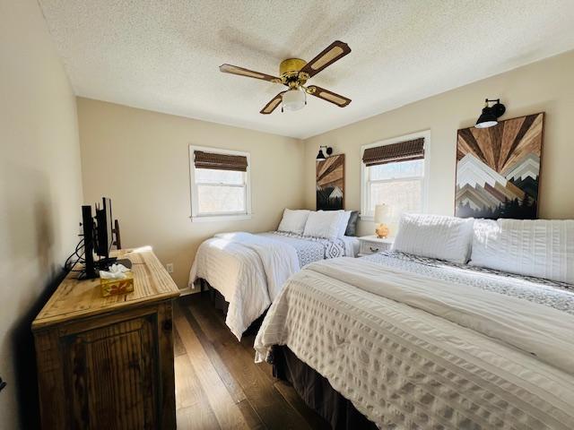 bedroom with a textured ceiling, dark wood-type flooring, and ceiling fan