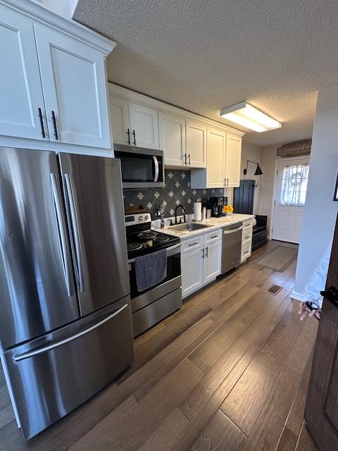 kitchen with dark wood-style flooring, light countertops, appliances with stainless steel finishes, white cabinets, and a sink