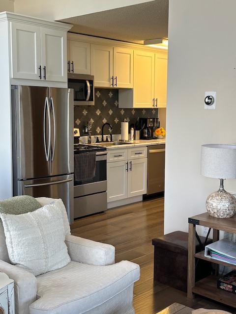 kitchen featuring backsplash, wood finished floors, stainless steel appliances, light countertops, and a sink