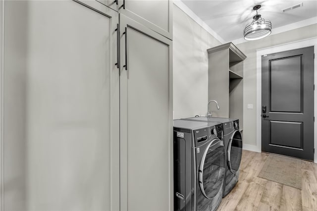 laundry room with cabinets, washing machine and clothes dryer, ornamental molding, and light hardwood / wood-style floors