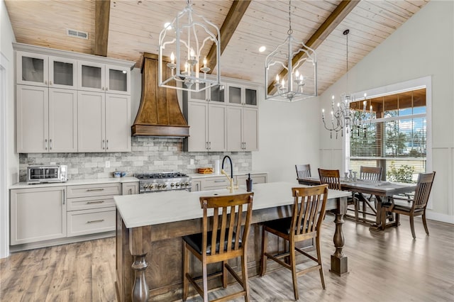 kitchen featuring range, hanging light fixtures, wooden ceiling, beamed ceiling, and a kitchen island with sink