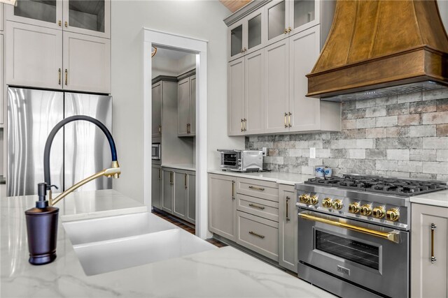 kitchen with custom exhaust hood, light stone countertops, appliances with stainless steel finishes, and gray cabinetry