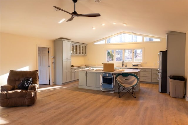 kitchen with gray cabinets, stainless steel fridge, a kitchen breakfast bar, a center island, and vaulted ceiling