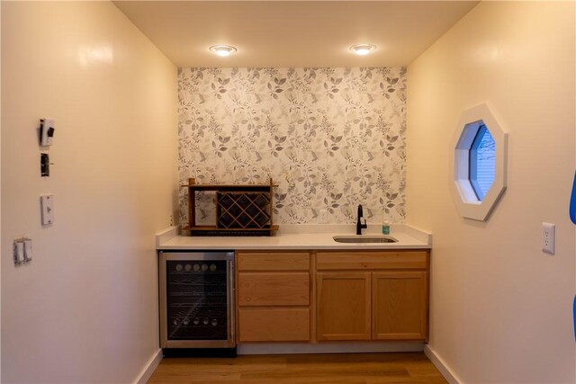 bar with beverage cooler, sink, and light wood-type flooring