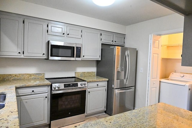 kitchen featuring washer / dryer, light stone countertops, appliances with stainless steel finishes, and gray cabinets