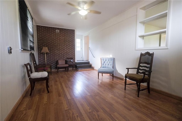 sitting room featuring brick wall, dark hardwood / wood-style floors, and ceiling fan