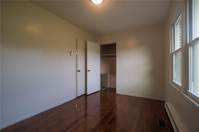 unfurnished bedroom featuring dark hardwood / wood-style floors, a closet, and baseboard heating