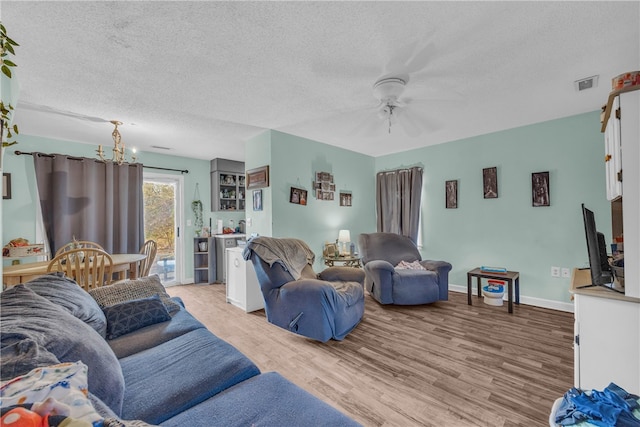 living room featuring ceiling fan with notable chandelier, a textured ceiling, and light hardwood / wood-style flooring