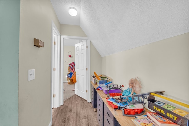 recreation room with hardwood / wood-style floors, vaulted ceiling, and a textured ceiling