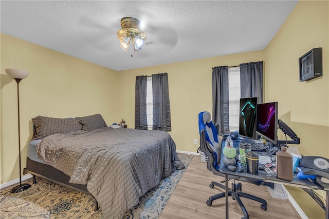 bedroom with a textured ceiling, ceiling fan, and light hardwood / wood-style flooring