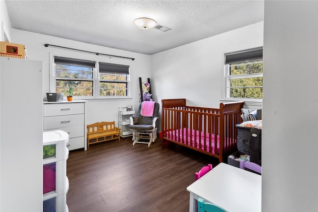 bedroom with multiple windows, dark wood-type flooring, a nursery area, and a textured ceiling