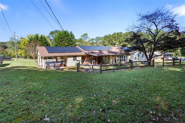 rear view of property featuring a lawn and solar panels