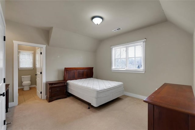 bedroom featuring multiple windows, lofted ceiling, ensuite bathroom, and light carpet