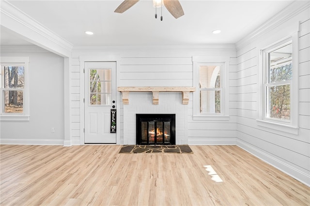 unfurnished living room featuring ceiling fan, ornamental molding, light hardwood / wood-style floors, and a brick fireplace