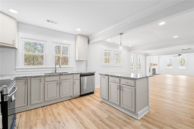 kitchen with sink, appliances with stainless steel finishes, hanging light fixtures, light stone countertops, and a kitchen island