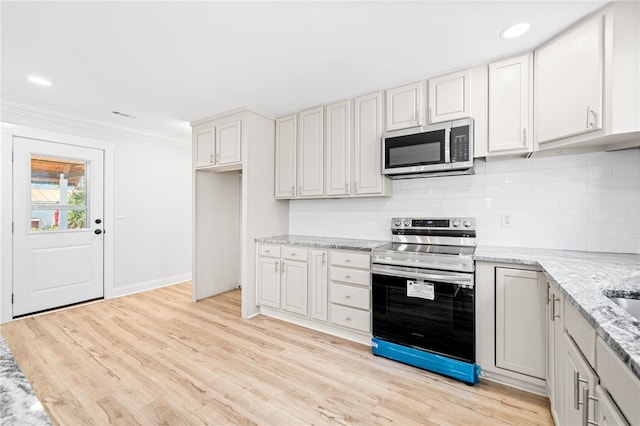 kitchen with appliances with stainless steel finishes, white cabinetry, decorative backsplash, ornamental molding, and light stone counters