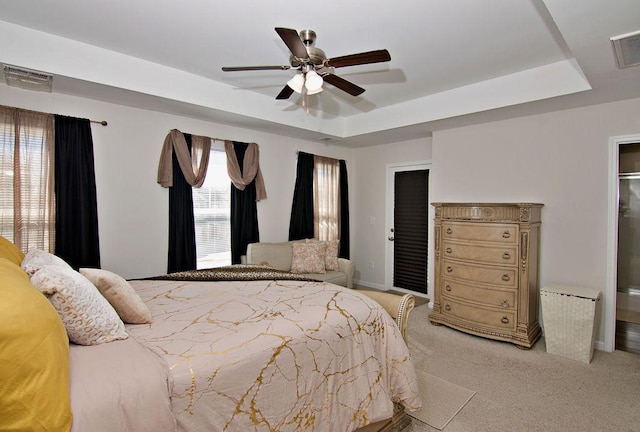 carpeted bedroom with a raised ceiling and ceiling fan