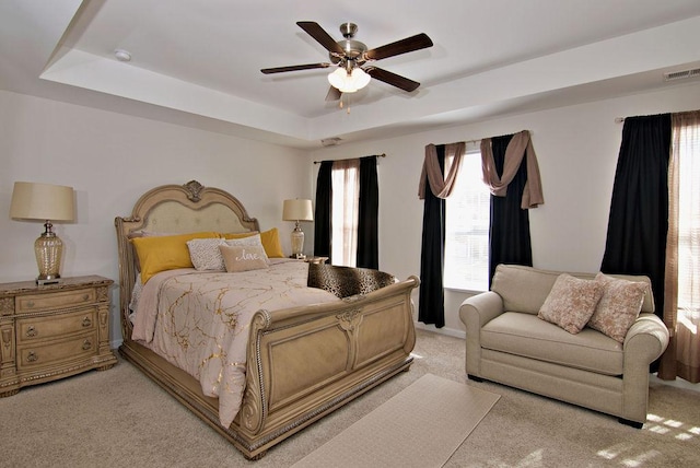 bedroom with light colored carpet, a raised ceiling, and ceiling fan