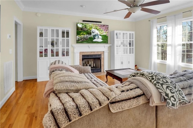 living room with ceiling fan, ornamental molding, light hardwood / wood-style floors, and a tile fireplace