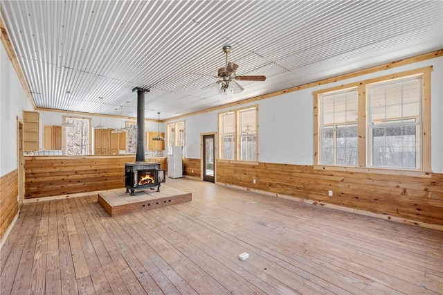 interior space featuring ceiling fan, a wood stove, wooden walls, and light wood-type flooring