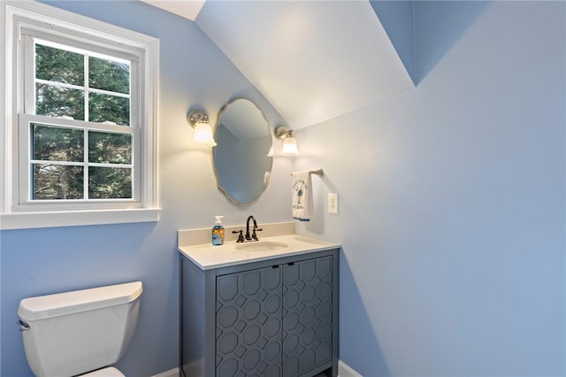 bathroom with a healthy amount of sunlight, vanity, vaulted ceiling, and toilet