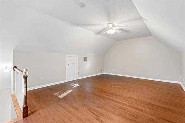 additional living space with hardwood / wood-style flooring, vaulted ceiling, a textured ceiling, and ceiling fan