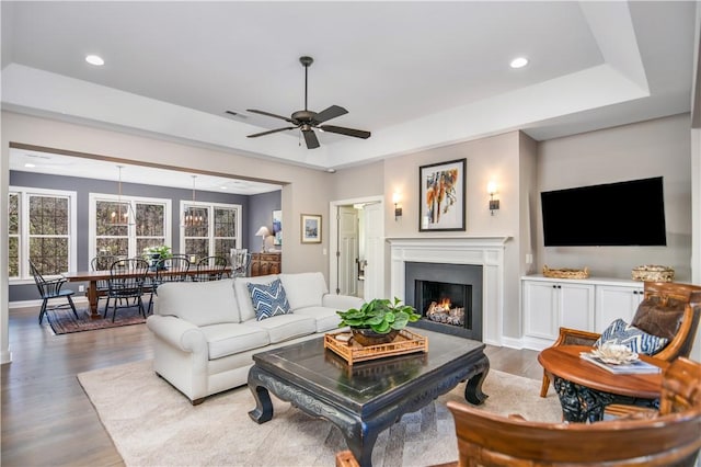 living room featuring a raised ceiling, ceiling fan, and light hardwood / wood-style flooring