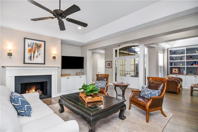 living room with built in shelves, wood-type flooring, french doors, and ceiling fan