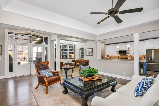 living room featuring decorative columns, a tray ceiling, hardwood / wood-style floors, and french doors