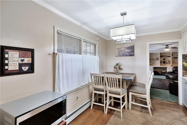 dining space featuring built in shelves, a baseboard radiator, ornamental molding, and light wood-type flooring