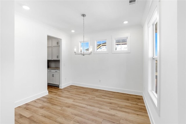 unfurnished dining area with crown molding, light wood-type flooring, and a notable chandelier