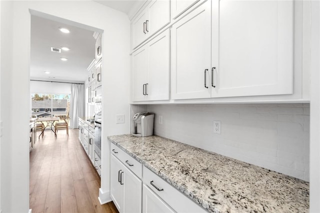 kitchen with tasteful backsplash, white cabinetry, light stone counters, and light hardwood / wood-style floors