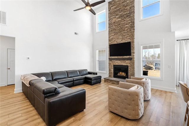 living room with a stone fireplace, ceiling fan, and light hardwood / wood-style flooring