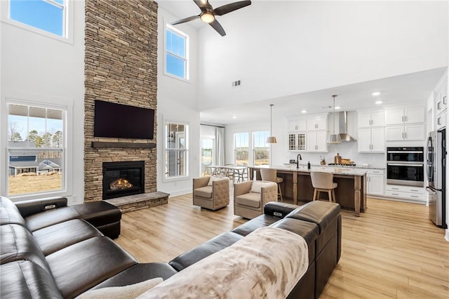 living room with sink, a stone fireplace, light hardwood / wood-style floors, and ceiling fan