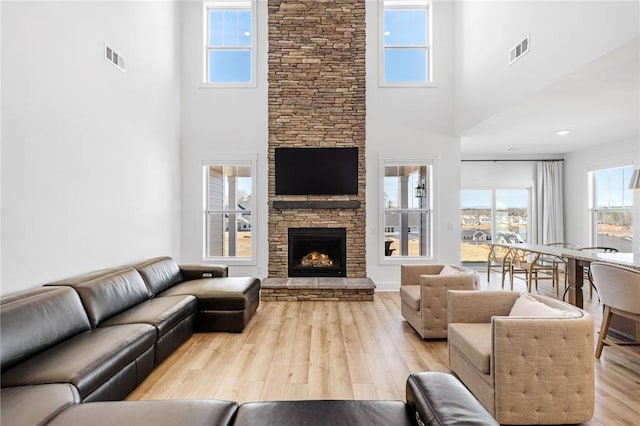 living room featuring a towering ceiling, a fireplace, and light hardwood / wood-style flooring