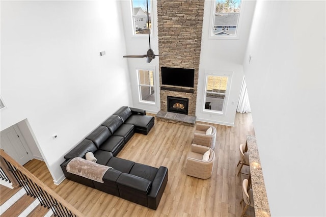 living room with hardwood / wood-style flooring, a stone fireplace, a high ceiling, and plenty of natural light