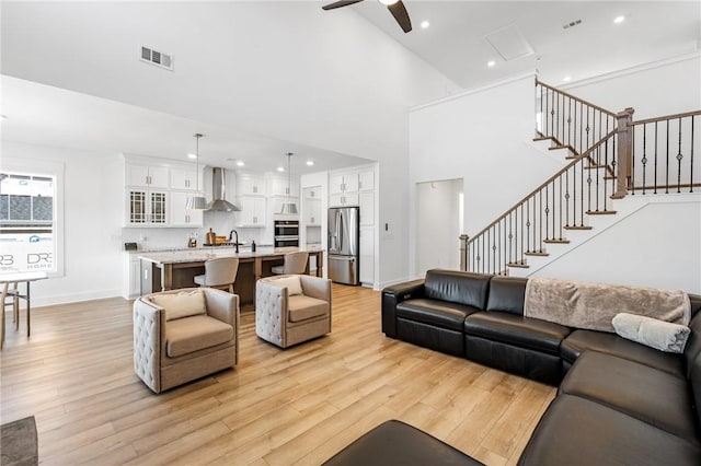 living room featuring a towering ceiling, sink, ceiling fan, and light hardwood / wood-style flooring